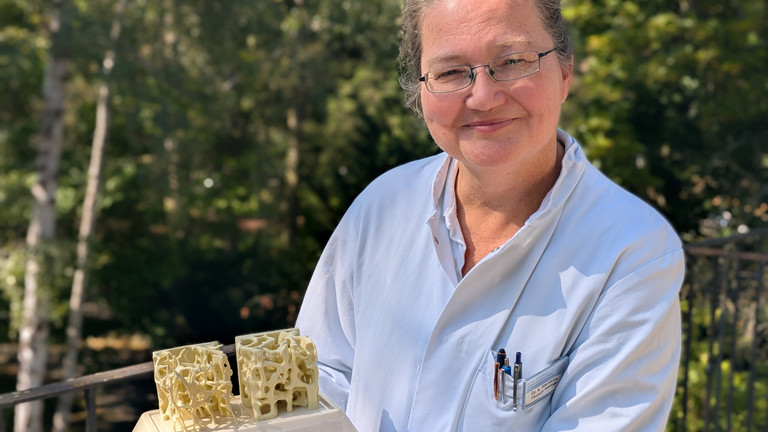 Dr. med. Katja Warnecke steht auf einem Balkon mit einem Modell in der Hand 