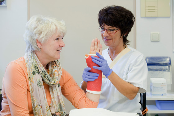 Auf dem Foto sieht man eine Pflegekraft die den Gipsarm einer Patientin hoch hält Auf dem Foto sieht man eine Pflegekraft die den Gipsarm einer Patientin hoch hält