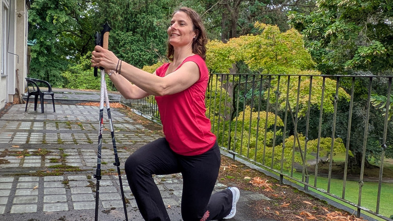 Therapeutin führt Übung mithilfe von Nordic Walking Stöcken aus