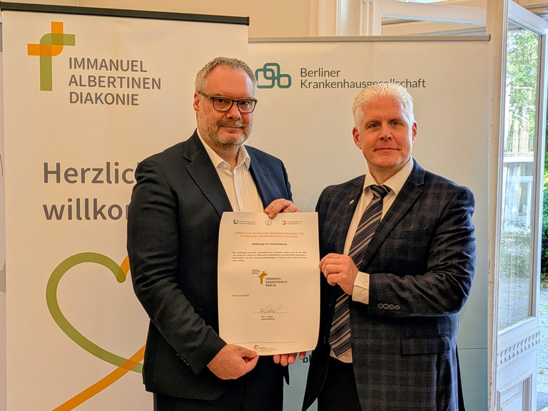 Roy J. Noack, Geschäftsführer des Immanuel Krankenhaus Berlin und Marc Schreiner, Geschäftsführer der Berliner Krankenhausgesellschaft halten die unterschriebene BKG-Charta Urkunde ins Bild