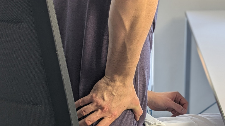 Mann sitzt auf Stuhl und hält Hand an unteren Rücken