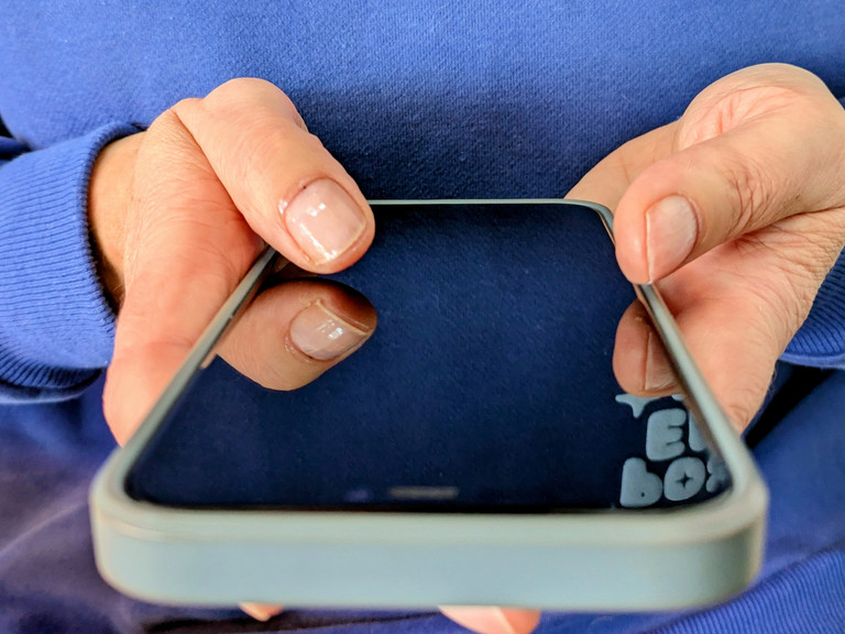Person hält Smartphone in den Händen und hält beide Daumen auf Bildschirm